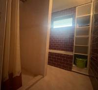 Bathroom with tiles, shower enclosure, and a shelf in a family house.