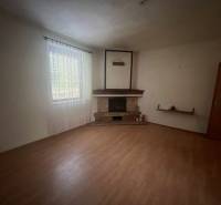 Spacious room in a family house with a fireplace, wooden-patterned flooring, and a large window.