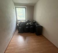 A narrow room in a family house with a wooden-decor floor and bags by the window.