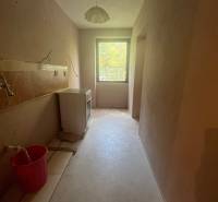 A narrow room in a family house with a single-pane window and a ceiling light, in need of renovation.