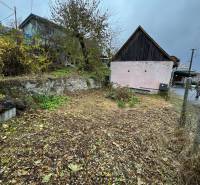 A family house in Plášťovce with a garden, trees, and a stone retaining wall.
