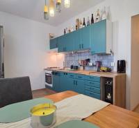 A kitchen in a 3-room apartment with a turquoise kitchen unit and a wooden decor floor.