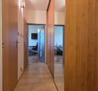 A hallway with a wooden decor floor, a mirrored wardrobe, and a view into a 3-room apartment.