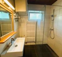 A bathroom in a family house with a shower, a sink, and a window, with a wooden decor floor.