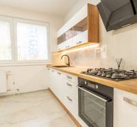 A kitchen in a 3-room apartment with a gas stove, wooden decor, and white cabinets.