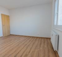 A room in a 3-room apartment with a wooden decor floor, white walls, and a radiator.
