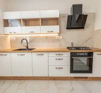 A kitchen with white cabinets, a black range hood, a cooktop, and a floor with a wood design.