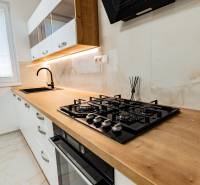 A kitchen in a 3-room apartment with a wood-patterned floor, a built-in cooktop, and a wooden countertop.
