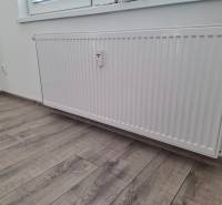 Radiator by a white wall, next to a floor with wood decor in a 3-room apartment.
