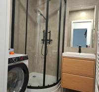 Bathroom in a 3-room apartment with a washing machine, shower, and sink with storage space.