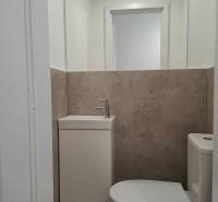 Bathroom in a 3-room apartment with a sink and toilet, neutral-colored tiles.