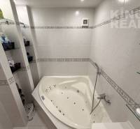 A bathroom in a 3-room apartment with a corner bathtub and shelves for cosmetics.
