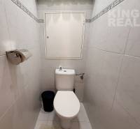 A toilet in a 3-room apartment with white tiles and a toilet paper holder.