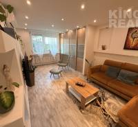 Living room in a three-room apartment with wooden floor decor, a sofa, and flower pots.