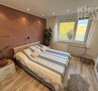 A bedroom in a 3-room apartment with a wooden decor floor and a plant next to the bed.