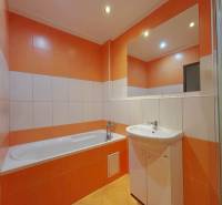 A bathroom with a bathtub and a sink in a 3-room apartment with orange and white tiles.