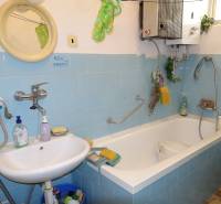 A bathroom with blue tiles and a white bathtub in a family house.