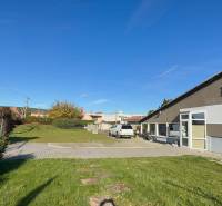 Commercial premises in Dolné Chlebany with a parking lot, landscaped greenery, and a blue sky.