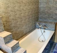 A bathroom with a bathtub in a 2-room apartment, tiled with patterned tiles.