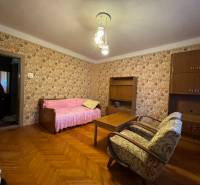 The living room in the family house has wallpapered walls, wooden furniture, and a floor with a wooden decor.