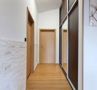 A hallway with white walls, a large mirror, and a wooden decor floor in a family house.