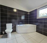 A bathroom in a family house with a bathtub, toilet, and black tiles.