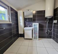 A bathroom in a family house with black tiles and a boiler, floor with light tiles.