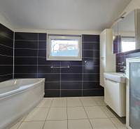 A bathroom in a family house with a bathtub, dark tiles, and white flooring.
