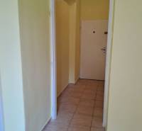 A hallway in a one-room apartment with light tiles and yellow walls.
