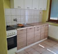 A kitchen in a studio apartment with white cabinets and tiled flooring.