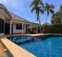 A villa in Pattaya with a garden and a pool, surrounded by palm trees and a hedge.