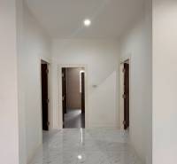 A white hallway in a villa with a marble-like floor and three doors.