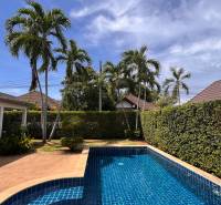 Villa in Pattaya with a pool, palm trees, and a landscaped garden on a sunny day.