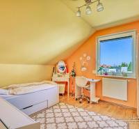Attic room with a bed, a desk, and a wooden-patterned floor in a family house.