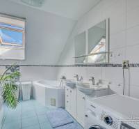 Bathroom with a window, bathtub, two sinks, and a washing machine in a family house.