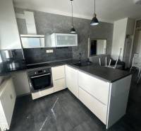 A kitchen in a studio apartment with a dark countertop, gray wall, and pendant lighting.