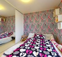A colorful bedroom with zebra wallpaper, patterned bed linen, and a mirrored wardrobe in a four-room apartment.