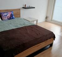 A bedroom in a studio apartment with a bed, an armchair, and a wooden decor floor.