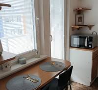 A kitchen with a dining area, a microwave, and windows with blinds in a studio apartment.