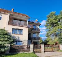 A family house in Hronské Kosihy, with two balconies, a garden, and trees on the property.