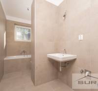 Bathroom in a 2-room apartment with a bathtub, sink, and window. Light tiles.