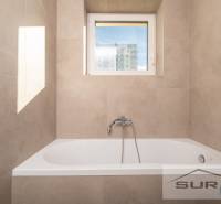 A bathtub with a built-in faucet and a window in a 2-room apartment with warm-toned tiles.