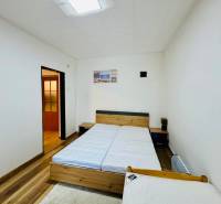 A room in a cottage with two beds, white walls, and a floor with a wooden decor.