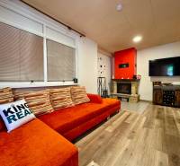 Living room with an orange sofa, fireplace, television, and wooden decor flooring in a cabin.
