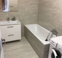 Bathroom with light tiles, bathtub, sink, and washing machine in a studio apartment.