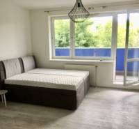 A bright room with a bed, an open balcony, and a floor with a wooden decor.