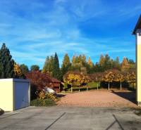 The courtyard of a family house in Necpaly with a paved area and a green background.