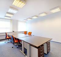 An office with desks, orange chairs, and windows with blinds.