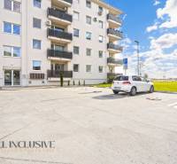 Parking lot in front of the apartment building on Panónsky háj in Dunajská Streda, with cars and a grassy area.