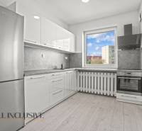 A kitchen with a wood-patterned floor in a 2-room apartment with modern furnishings.